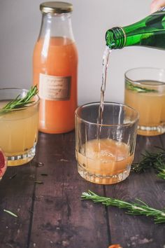 two glasses filled with orange juice and some rosemary sprigs are being poured into them