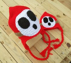 a crocheted red hat with black and white panda ears on the top, attached to a wooden post