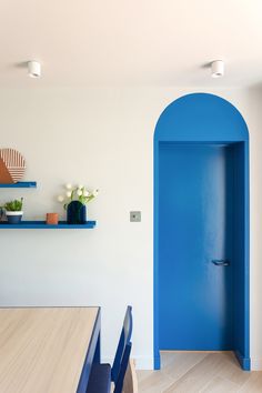 an open blue door in the middle of a room with wooden flooring and white walls