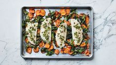 a pan filled with fish and veggies on top of a marble counter