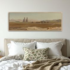 a painting hanging above a bed with white sheets and pillows on it's headboard