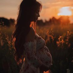 a pregnant woman standing in a field at sunset