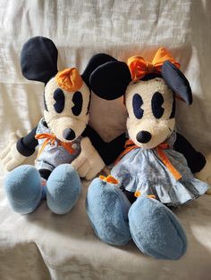 two stuffed animals sitting on top of a white couch next to each other with orange bows