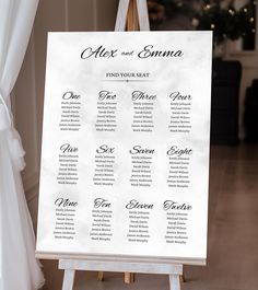 an easel with a seating chart on it in front of a christmas tree and white drapes