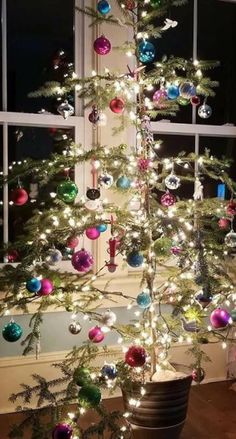 a small christmas tree with ornaments on it in front of a window and a potted plant