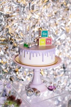 a cake with purple icing and colorful blocks on top sitting in front of a christmas tree