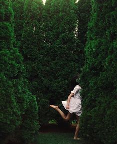 a woman in white dress standing between two tall green bushes with her legs spread out