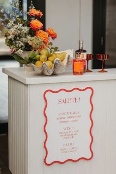 a white counter topped with lots of fruit and flowers next to a sign that says salute cocktails