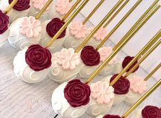 there are many cupcakes with pink and red frosting on the top, along with gold sticks