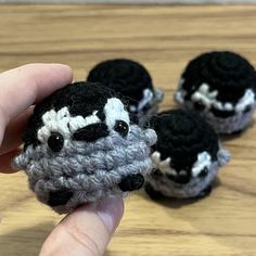 someone is holding three small crocheted sheeps on a wooden table with their fingers