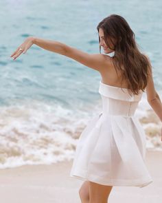 a woman in a white dress is on the beach with her arms out and one arm extended