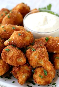 some fried food on a white plate with ranch dip in the middle and garnished with parsley