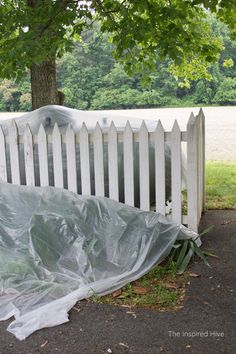 a white bench covered with plastic sitting in the grass next to a tree and fence