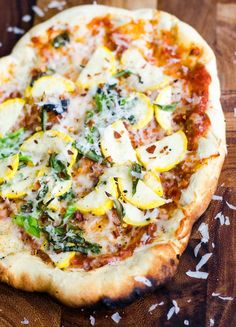 a pizza sitting on top of a wooden table covered in cheese and veggies