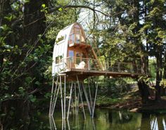 a house built on stilts in the middle of a lake surrounded by trees and greenery