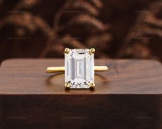 an emerald cut diamond ring sitting on top of a wooden box in front of a brown background