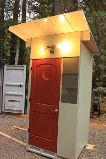 a red and white outhouse sitting in the middle of a forest