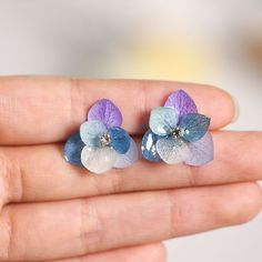 two small blue and white flowers are in someone's hand, one is wearing a pair of earrings