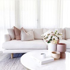 a living room with white couches and flowers in vases on the coffee table