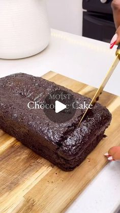 a person cutting into a chocolate cake on a wooden cutting board with a yellow handled knife