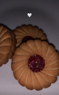 three cookies with jam on them sitting next to each other in front of a white heart