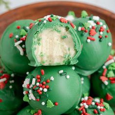 green cake balls with white frosting and sprinkles on them in a wooden bowl