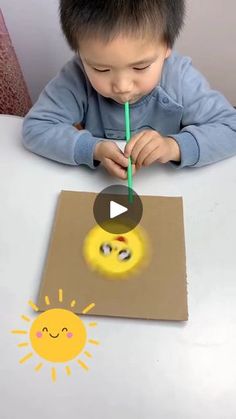 a young boy sitting at a table with a pencil in his mouth and an image of a smiley face