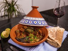 a bowl filled with food sitting on top of a table next to a glass of wine