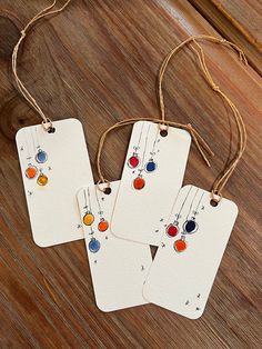 three tags are hanging from string on a wooden surface with strings attached to them and colorful beads in the middle