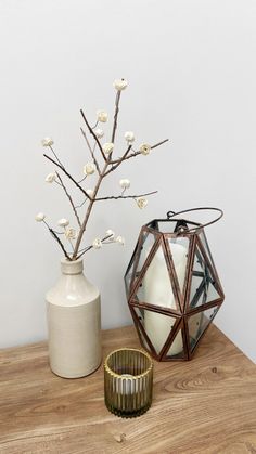 two vases with white flowers are sitting on a table next to a candle holder