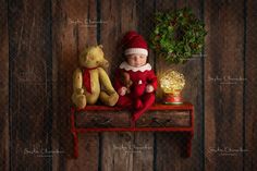 a baby dressed as santa claus sitting on a table next to a teddy bear and christmas wreath