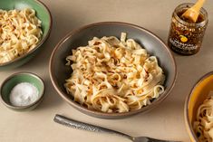 two bowls filled with pasta next to spoons and salt