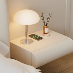 a white table with a lamp and cell phone on it, next to a bed