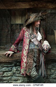 a man dressed in pirate costume standing next to a stone wall