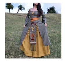 a woman in a long dress standing on top of a grass covered field