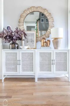 a white sideboard with wicker doors and a round mirror above it on the wall