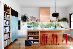 a woman sitting at a counter in a kitchen next to two stools and a book shelf