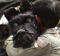 a man is hugging a dog in front of a car with it's head on his shoulders