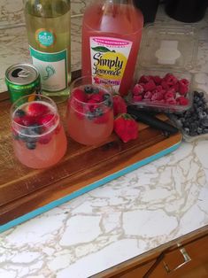 some drinks are sitting on a cutting board with strawberries and blueberries in it