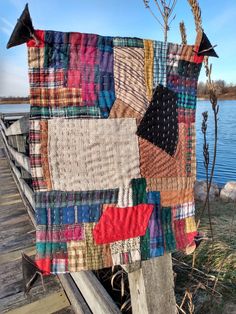 a patchwork quilt is hanging on a wooden post by the water's edge