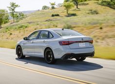 the rear end of a silver car driving down a road