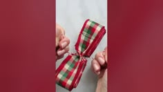 two hands holding a red and green plaid ribbon