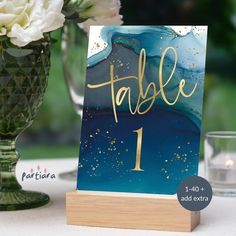 a table number sign sitting on top of a wooden stand next to a vase filled with flowers