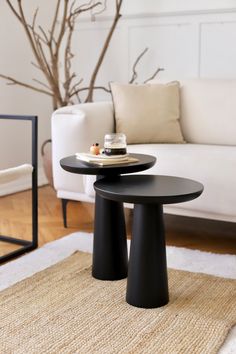 two black tables sitting on top of a rug in front of a white couch and coffee table