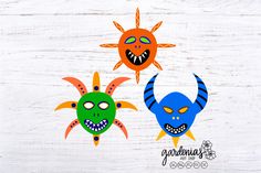 three masks with different designs on them are sitting on a white wooden surface, one has an evil face and the other is a monster's head