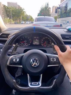 a person is driving a car with their hand on the steering wheel, and there are other cars in the background