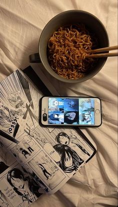 a bowl of noodles and chopsticks next to a cell phone on a bed