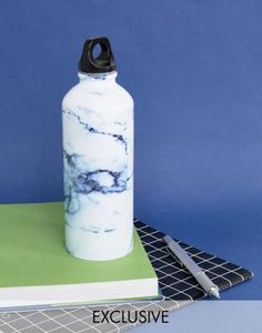 a white and black marbled water bottle next to a notebook