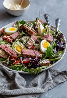 a salad with meat, eggs and vegetables in a white bowl on a gray table