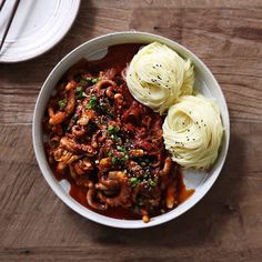 a bowl filled with noodles and meat on top of a wooden table